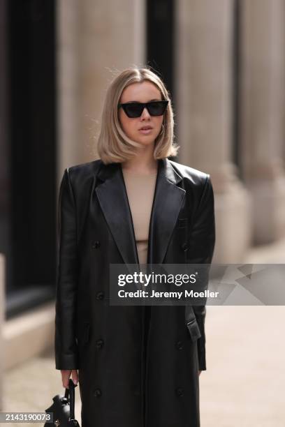 Isabelle Hartmann seen wearing Celine black sunglasses, vintage beige short dress and Magda Butrym black leather long coat on April 05, 2024 in...