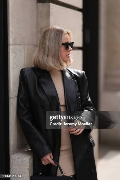 Isabelle Hartmann seen wearing Celine black sunglasses, vintage beige short dress and Magda Butrym black leather long coat on April 05, 2024 in...