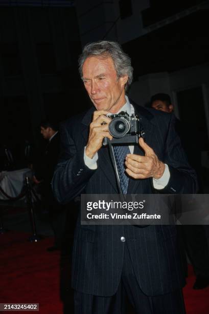 American actor and film director Clint Eastwood, holding a Nikon SLR camera, attends the Burbank premiere of 'The Bridges of Madison County', at...
