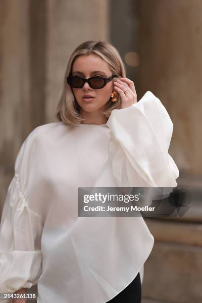 Isabelle Hartmann seen wearing Vehla Eyewear black / brown sunglasses, Nootka gold earrings, Khaite oversized puffy ruffled long sleeve silk top,...