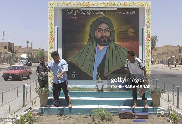 Iraqi men water the plants and lay tiles in front of a mural painting of Imam Ali, the cousin and son-in-law of Islam's Prophet Mohammed, in the...