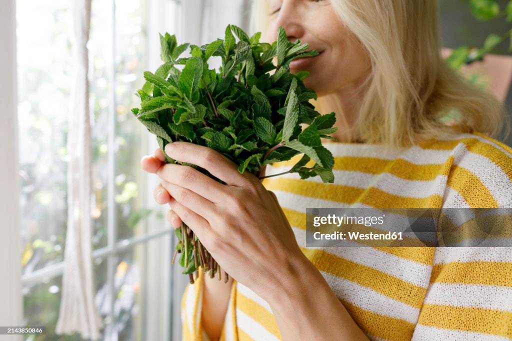 Mature woman smelling fresh mint at home