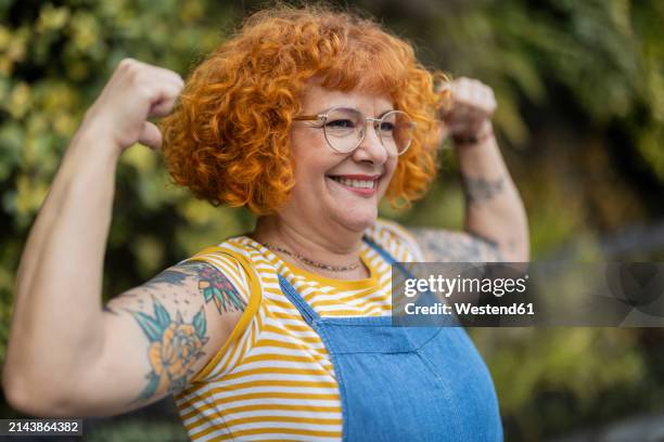 redhead woman with eyeglasses flexing muscles - flexing muscles stock pictures, royalty-free photos & images