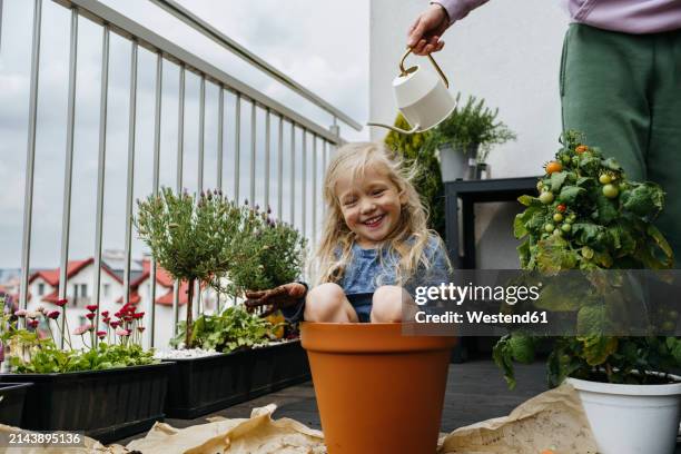 father watering playful girl sitting in pot at balcony - ukraine people stock pictures, royalty-free photos & images