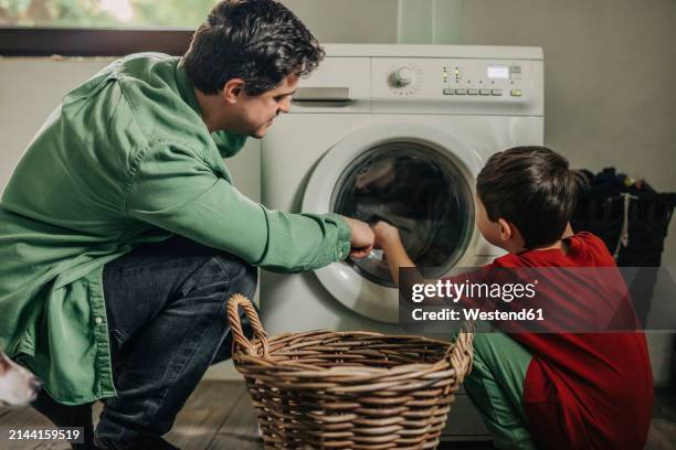 father and son loading clothes from basket in washing machine at home - man washing basket child stock pictures, royalty-free photos & images