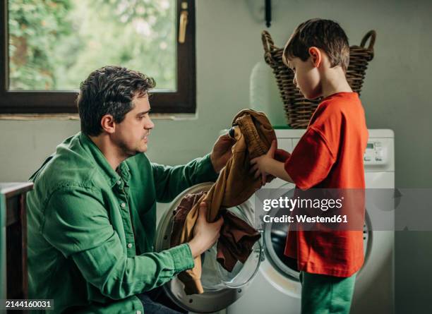 father and son removing clothes from washing machine at home - man washing basket child stock pictures, royalty-free photos & images