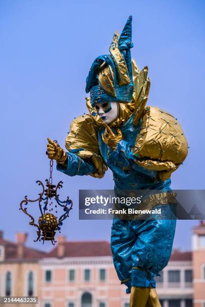 Masked person in a creative harlequin costume, posing at Canale Grande, celebrating the Venetian Carnival. The entire town Venice is part of the...