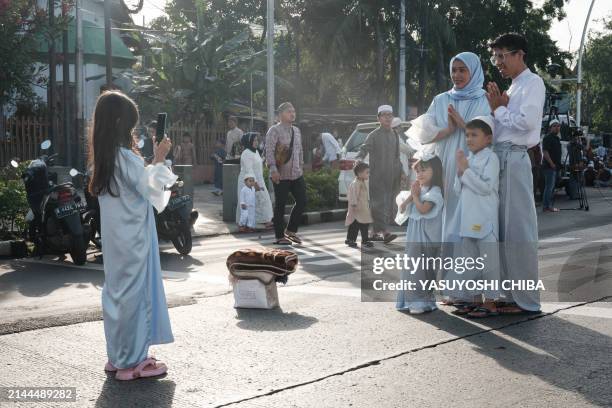 Muslim girl takes pictures of her family after Eid al-Fitr prayers, marking the end of the holy month of Ramadan, on a street in Jakarta on April 10,...
