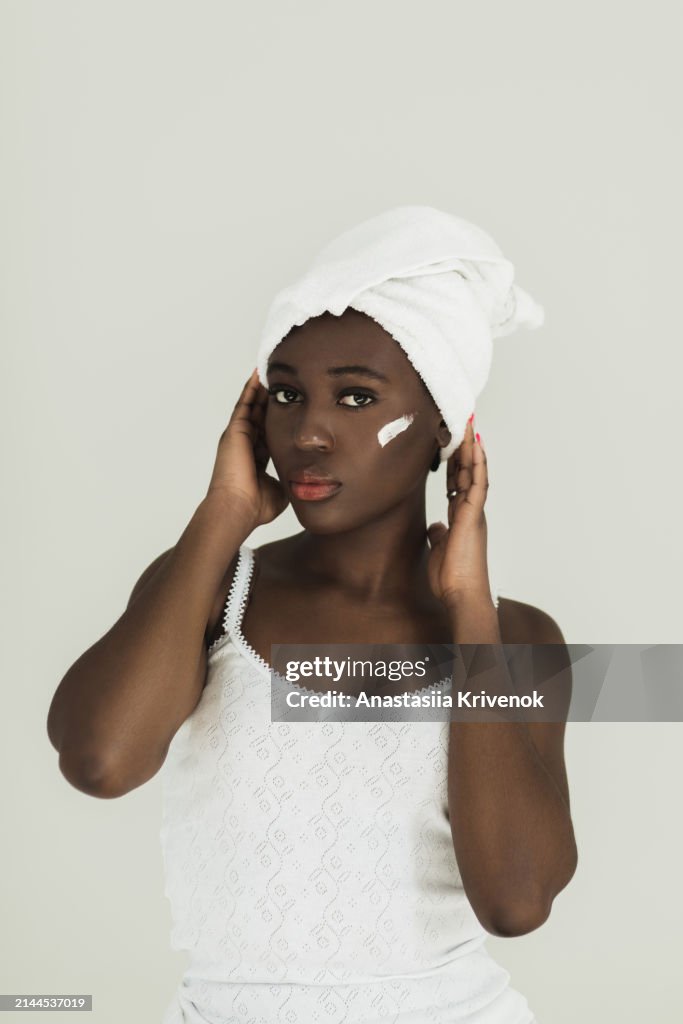 Smiling african american applying face cream on her perfect skin.
