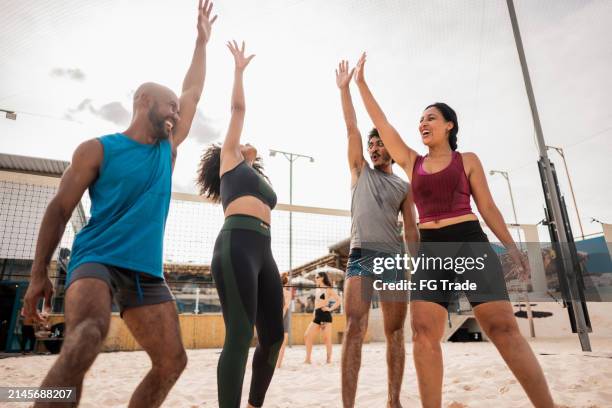 amici che festeggiano con le braccia alzate durante una partita di beach volley in un impianto sportivo - beach volley foto e immagini stock