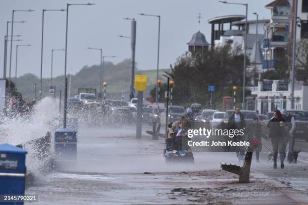 Woman gets hit with spray from a wave as she drives her mobility scooter in windy conditions along the seafront promenade in Westcliff on April 7,...