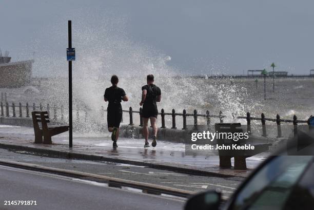 Joggers get hit by spray from a wave in windy conditions along the seafront promenade in Westcliff on April 7, 2024 in Southend-on-Sea, United...