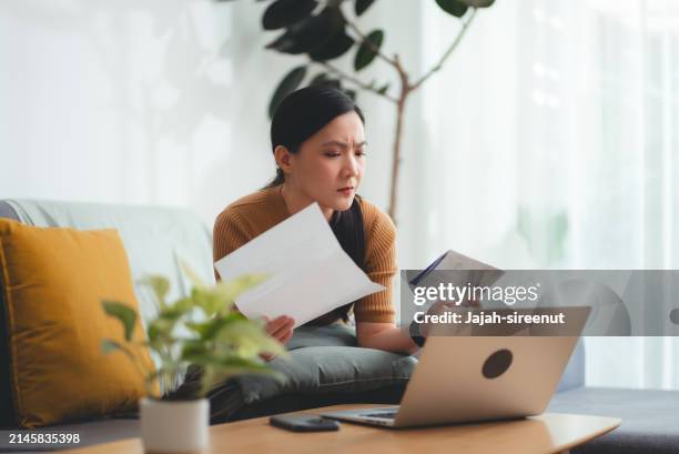 asian woman sitting on sofa worried having bill payment problems with bank papers mortgage debt and cost of living. - negative emotion stock pictures, royalty-free photos & images