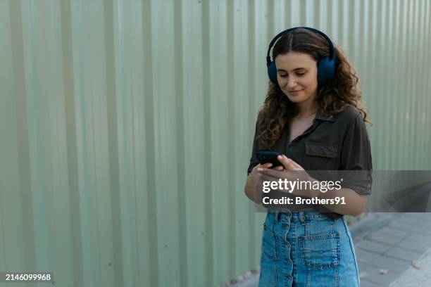 beautiful young woman using phone and listening to music on headphones - city life authentic stock pictures, royalty-free photos & images