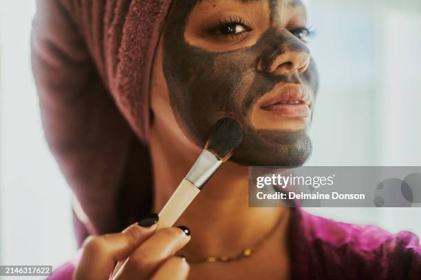 una mujer aplicando una mascarilla facial de carbón negro como parte de su rutina diaria de cuidado de la piel. - arcilla fotografías e imágenes de stock