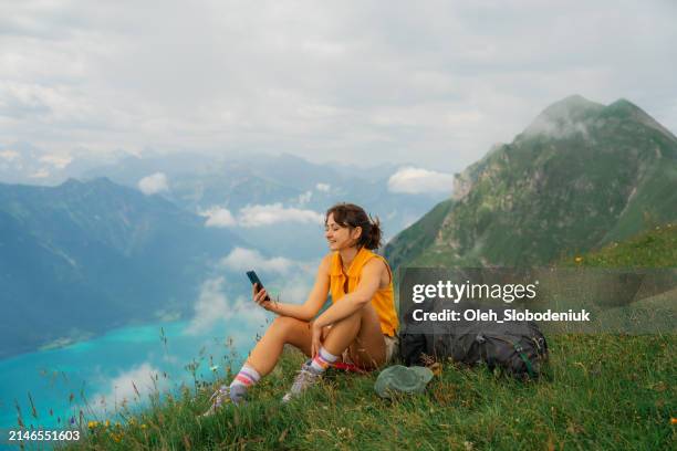 woman sitting on the meadow in swiss alps using smartphone during the hike - reisbestemmingen stockfoto's en -beelden
