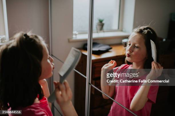 a pouting child combs her hair whilst looking in a mirror - girlie room stock pictures, royalty-free photos & images