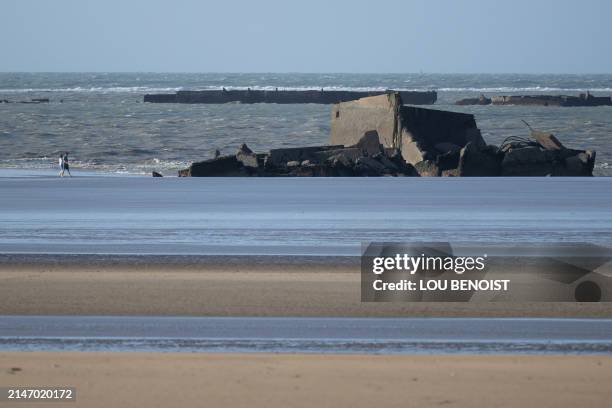 Tourist walk on the beach near remains of the British Artificial harbour, in Asnelles, on April 9 at "Gold Beach", a beach where some of the Normandy...