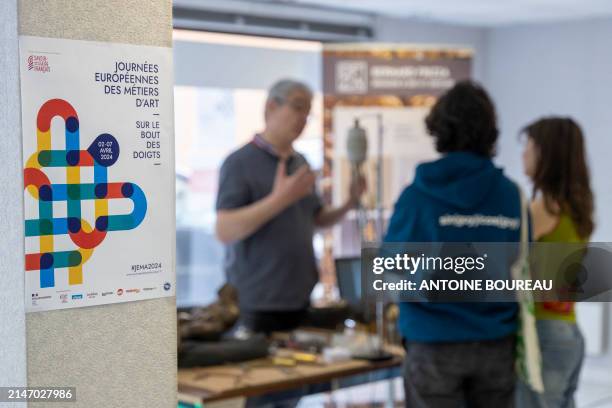 Poster and young couple talking to Bernard Frizzat, bronzesmith in Lyon, France on 7 April 2024. Photograph taken as part of the JEMA European Arts...