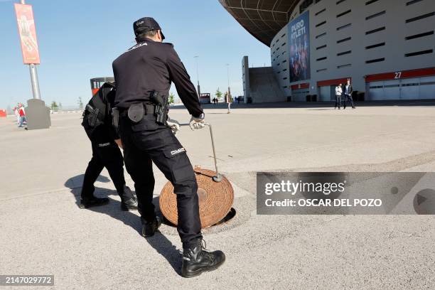 Spanish national police officers lift a manhole as they check the sewage system outside of the Metropolitano stadium prior to the UEFA Champions...