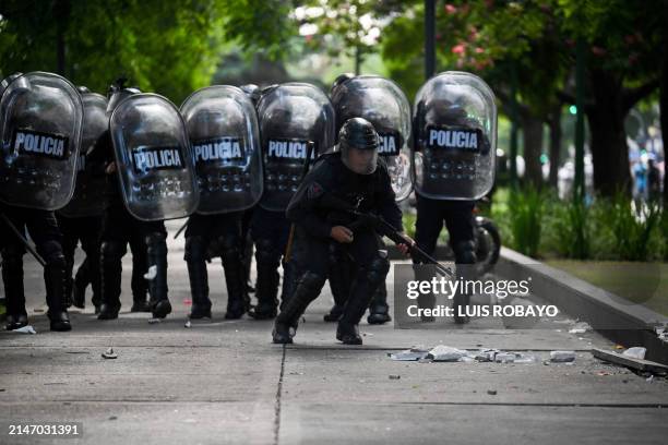 Police officer runs to aim a rubber bullet weapon against members of social organizations during a demonstration against the recent economic measures...