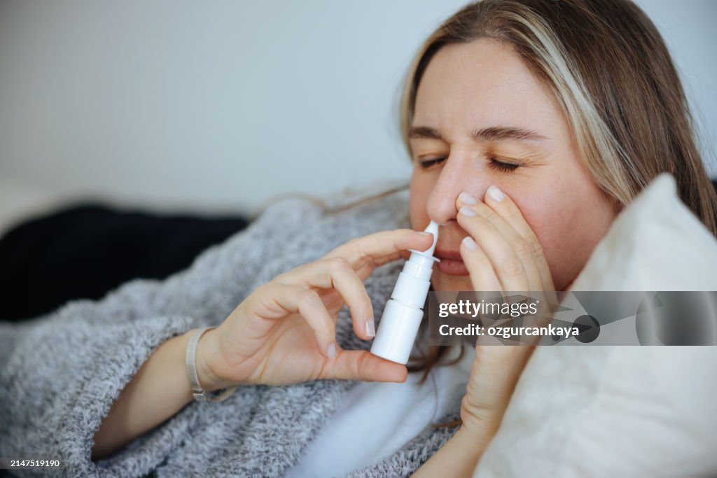 Sick young woman using nasal spray