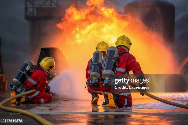 professional team firefighter supporting their team and spraying the high-pressure water to fire at the base of fire in the pipe tube, safety disaster accident and public service concepts. - roupa à prova de fogo imagens e fotografias de stock