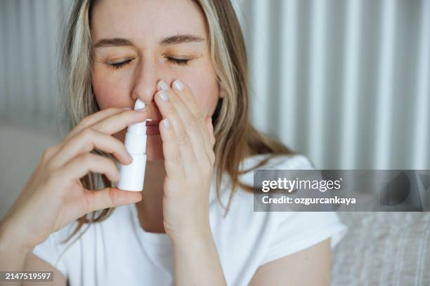 sick young woman using nasal spray - spray nasal imagens e fotografias de stock