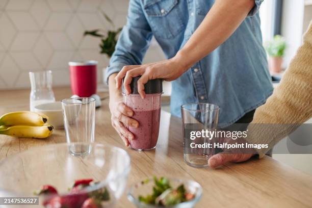 senior father and mature son making fruit smoothie as snack, having fun in kitchen. handsome man cutting strawberries on cutting board. - rührbesen stock-fotos und bilder