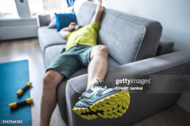 exhausting home training. tired man resting on sofa after the morning workout - luiheid stockfoto's en -beelden