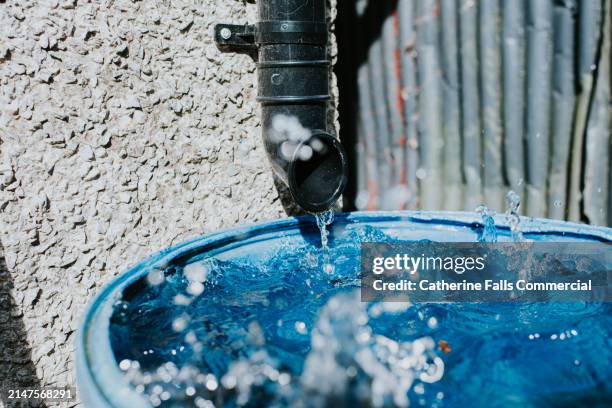 close-up of black plastic guttering draining into a large blue catchment basin - water pollution pipe stock pictures, royalty-free photos & images