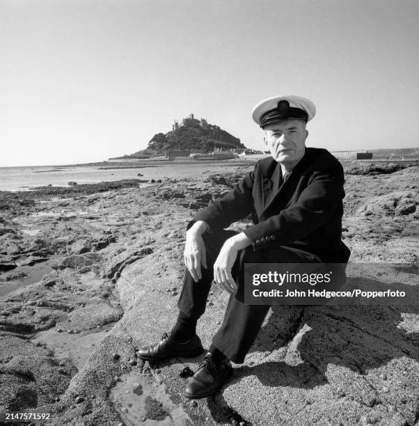 English peer and Royal Navy officer John St Aubyn, 4th Baron St Levan seated on the beach at Mount's Bay, with the family seat, St Michael's Mount...