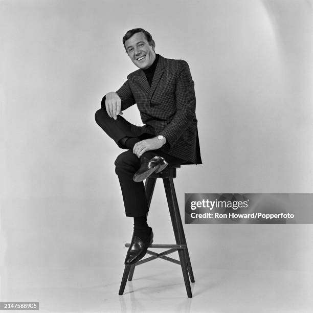 Irish singer Val Doonican posed seated on a stool in London circa 1970.