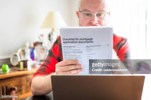 mid adult man reading mortgage application documents at home - legal documents stock pictures, royalty-free photos & images