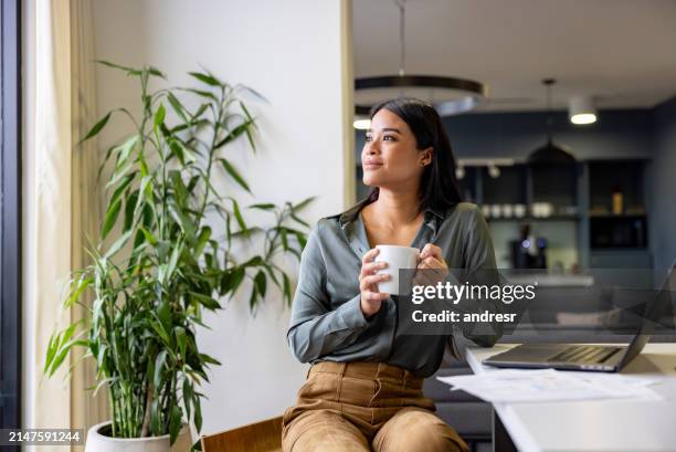 thoughtful businesswoman taking a break and drinking a cup of coffee - hispanic woman looking away stock pictures, royalty-free photos & images