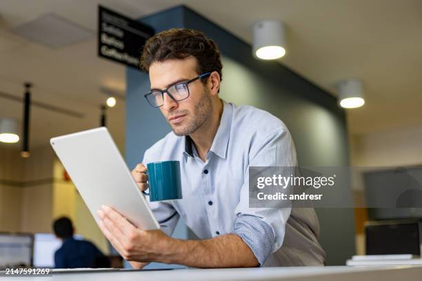 uomo d'affari che legge su una tavoletta digitale usando occhiali e bevendo caffè - occhiali da lettura foto e immagini stock