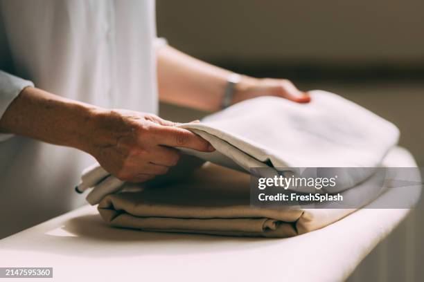 mature woman folding laundry at home with care - folded stock pictures, royalty-free photos & images