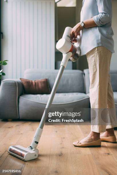 donna anziana che pulisce la casa con un aspirapolvere moderno - aspirapolvere foto e immagini stock