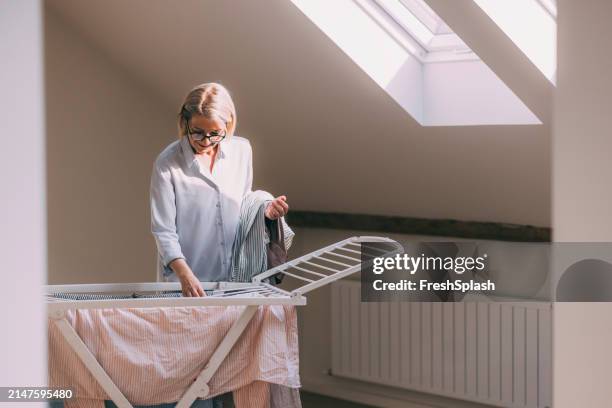 woman hanging clothes on drying rack indoors - drying rack stock pictures, royalty-free photos & images