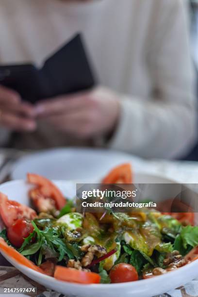 close-up of a plate of salad, behind it you can see some hands using a mobile phone - mjrodafotografia stock pictures, royalty-free photos & images