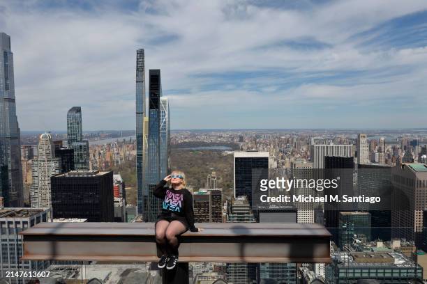 Laura Holden poses for a photo wearing eclipse glasses at the Beam as she prepares to watch a partial solar eclipse from the Top of the Rock at...