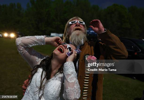 Bride and groom view the solar eclipse amid a darkened sky after marrying at a mass wedding at the Total Eclipse of the Heart festival on April 8,...