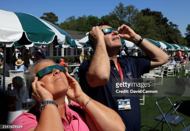 Sir Nick Faldo of England and his former caddie Fanny Sunesson of Sweden use pairs of special Masters 'eclipse' glasses to view the 75% eclipse...