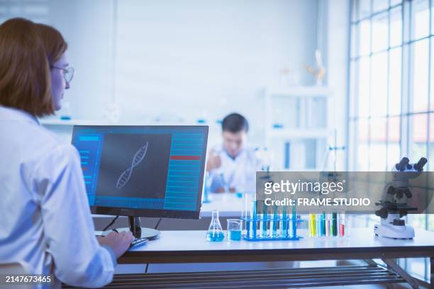 scientist analyzing data on computer in laboratory with microscope and test tubes, colleague working in background. research and science concept. - data science students fotografías e imágenes de stock