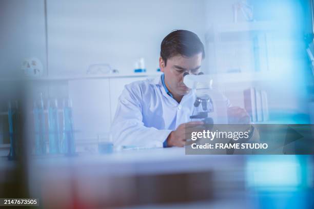 a scientist in a lab coat examining a sample under a microscope in a laboratory setting. - man microscope stock pictures, royalty-free photos & images