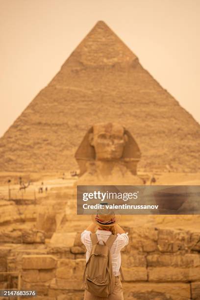 mujer de pie frente al fondo de las pirámides de giza y la esfinge y tomando fotos con el teléfono inteligente. giza, el cairo, egipto - esfinge fotografías e imágenes de stock