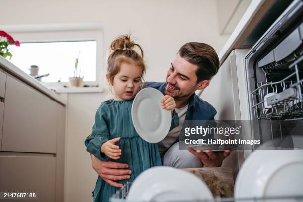 daughter helping father to clean kitchen after lunch, putting dirty dishes into dishwasher. - fathers day dinner stock pictures, royalty-free photos & images
