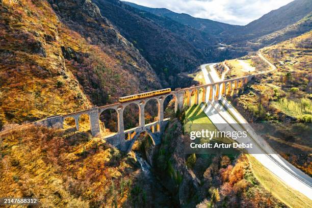aerial view of a yellow train crossing a stone bridge with dramatic landscape. the train jaune in france. - carruagem imagens e fotografias de stock