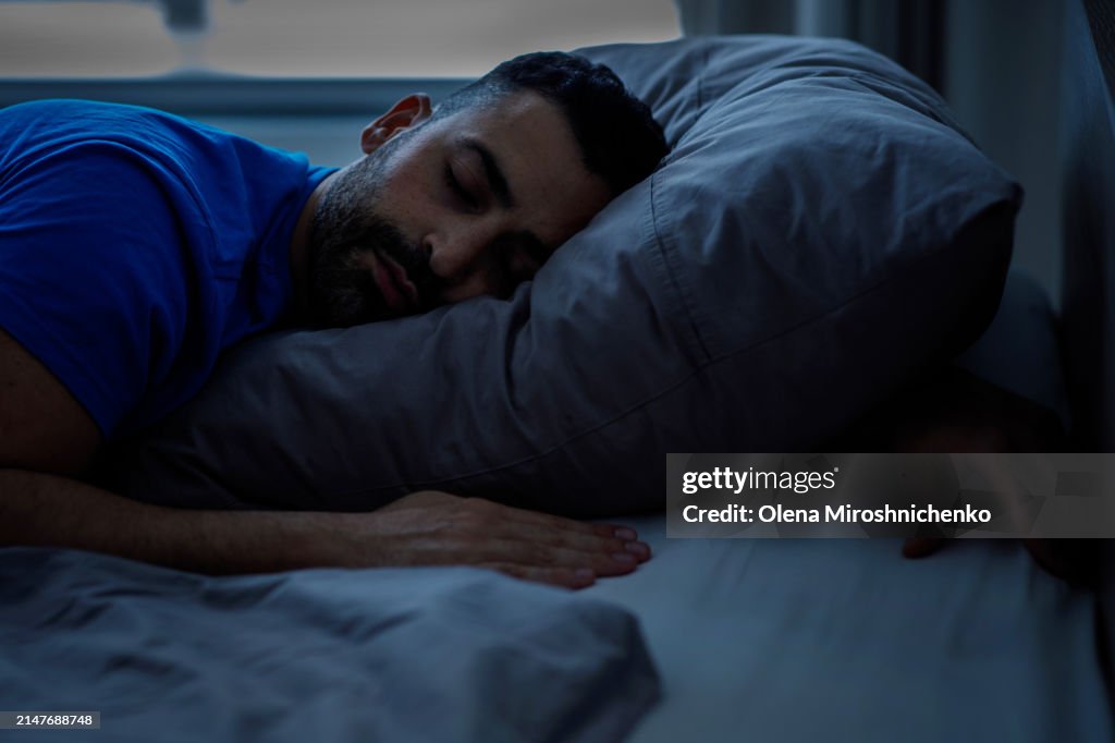 Sleeping young arab sleeping night, resting peacefully in a comfortable bed with gray linens with closed eyes, free space.
