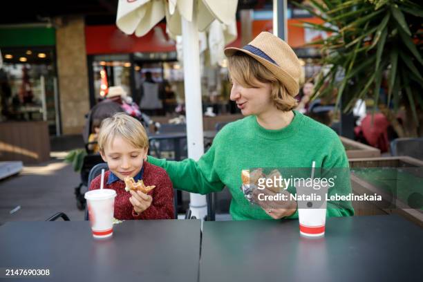 mom and blond kid sitting at table in street cafe eating chicken nuggets and french fries, enjoying fast food snack during travel - eating nuggets ストックフォトと画像